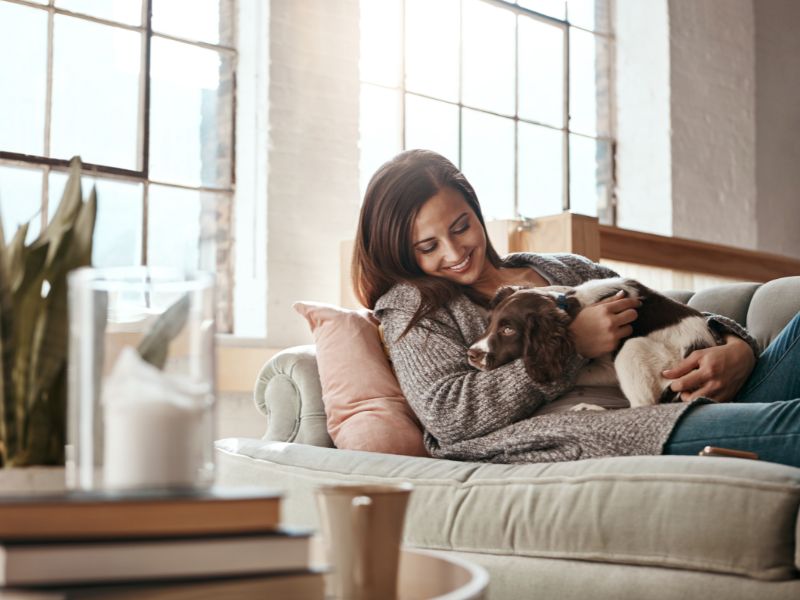 Happy woman sitting on a couch while hugging her dog