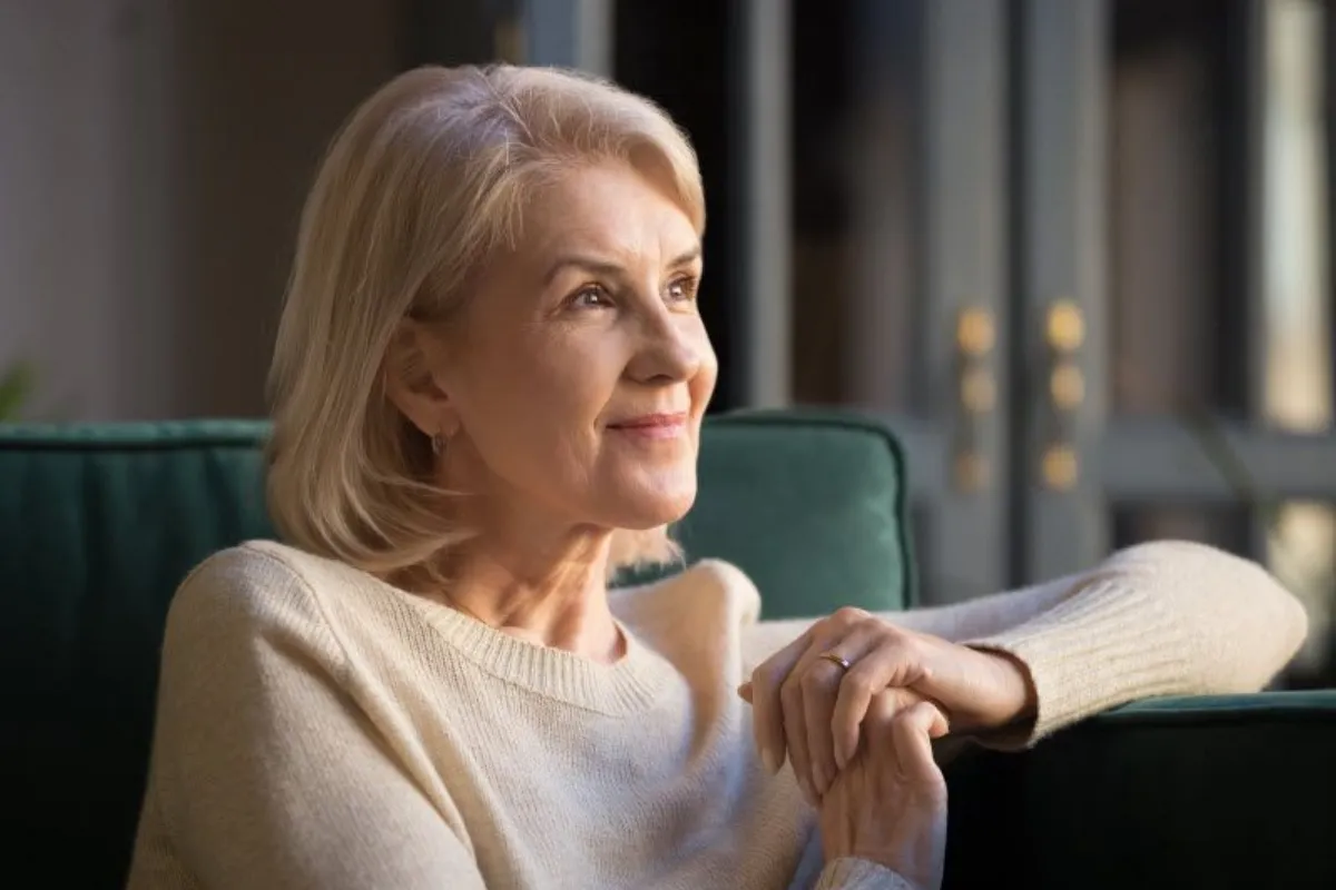 Smiling elderly woman look in distance while sitting on the couch
