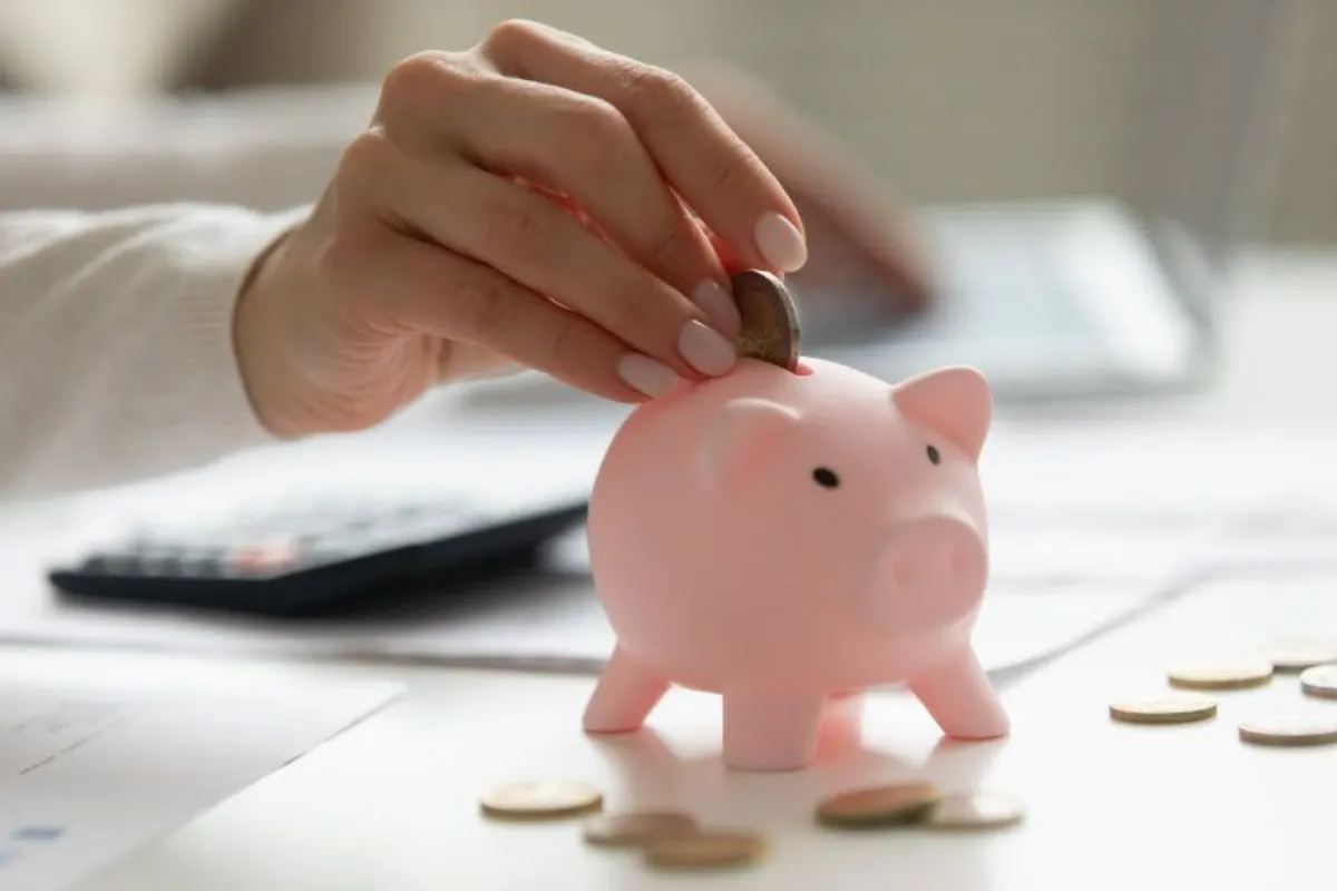 oman holding smartphone, putting coin in pink piggy bank,